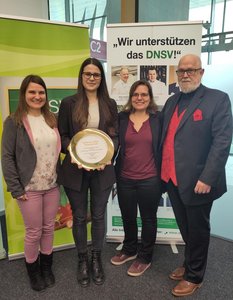 Dr. in Monika Reimer, Stine Möller, Dr.in Iris Lüschen und Dr. Michael Polster stehen vor einem Poster des DNSV. Stine Möller hält den Golden Teller in ihren Händen.Dr. in Monika Reimer, Stine Möller, Dr.in Iris Lüschen und Dr. Michael Polster stehen vor einem Poster des DNSV