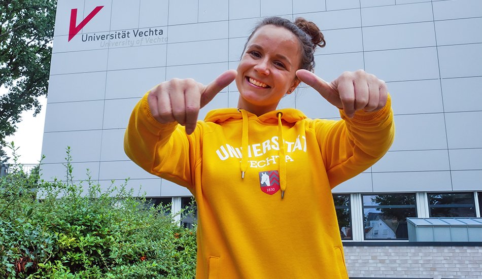 Studienangebot (Kreimer/Universität Vechta) Lächelnde Studentin im gelben Uni-Pullover zeigt beide Daumen nach oben