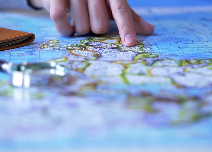 Auslandskompetenzen - Landkarte mit Lupe und ein Finger, der auf die Karte zeigt